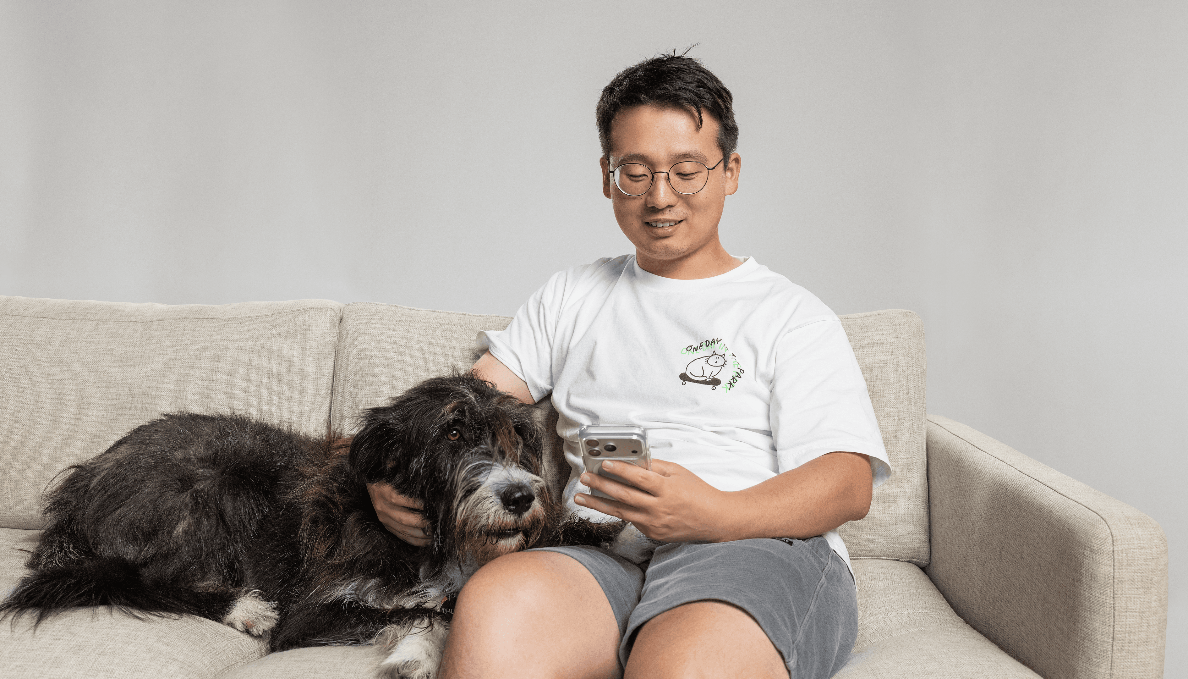 A man on a sofa looking at his phone with his dog beside him